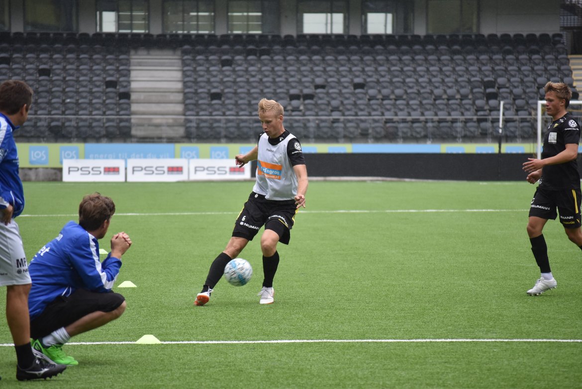 Simon Larsen slår en pasning, mens trenerne følger nøye med.